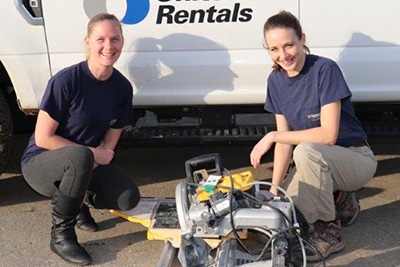 Apprentices Chelsea Short and Anne Lassere squatting by a circular saw