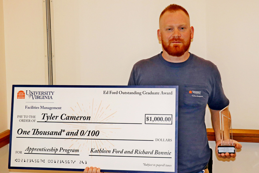 Tyler Cameron holds an oversized check for a thousand dollars and the Ed Ford Outstanding Graduate Award